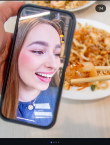 Modelka v telefonu se usmívá směrem na hůlky držící krevetu.